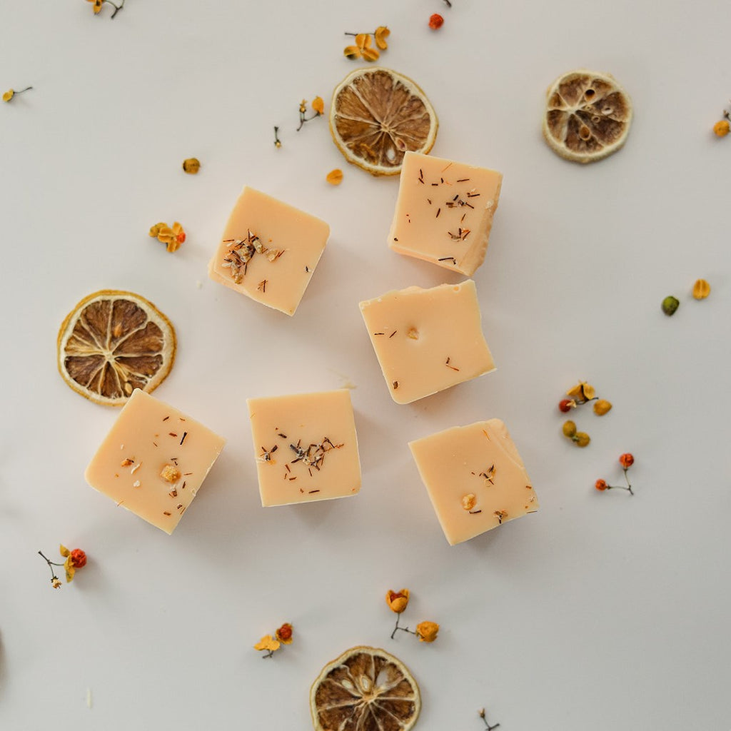 Orange Grove wax melt clamshell with fresh orange slices and yellow wildflowers on weathered wood surface