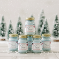 Six Frosted Snowman mini mason jar candles with gold lids standing upright on a wood surface in front of a snowy winter forest scene